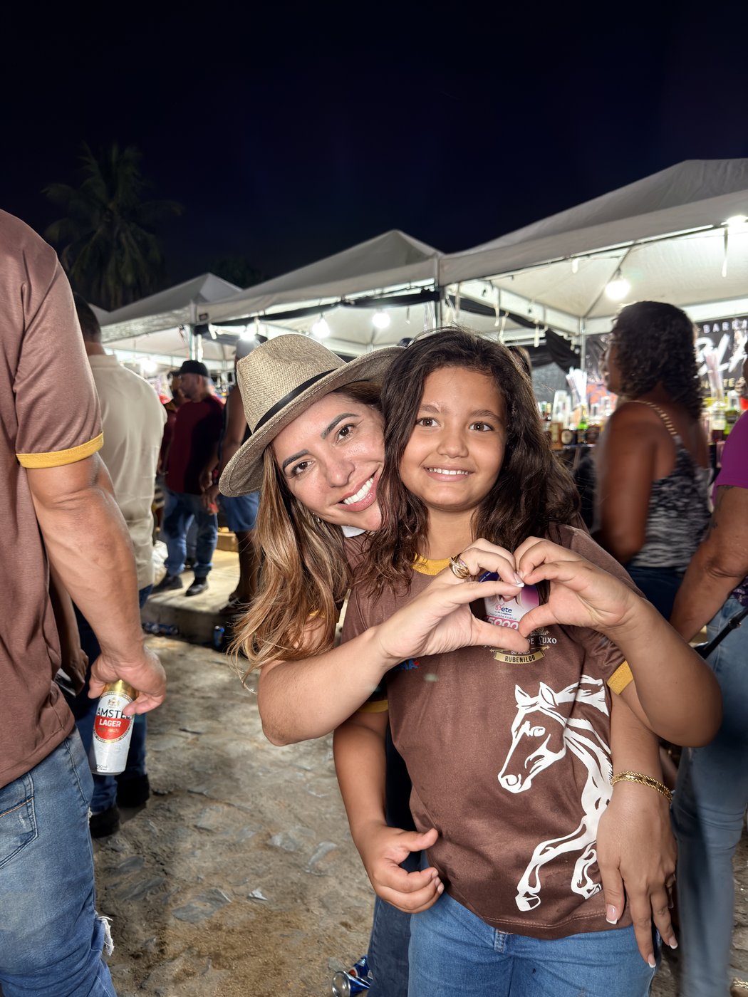 Bete abraçada a uma menina que faz um coração com as mãos, em festa noturna
